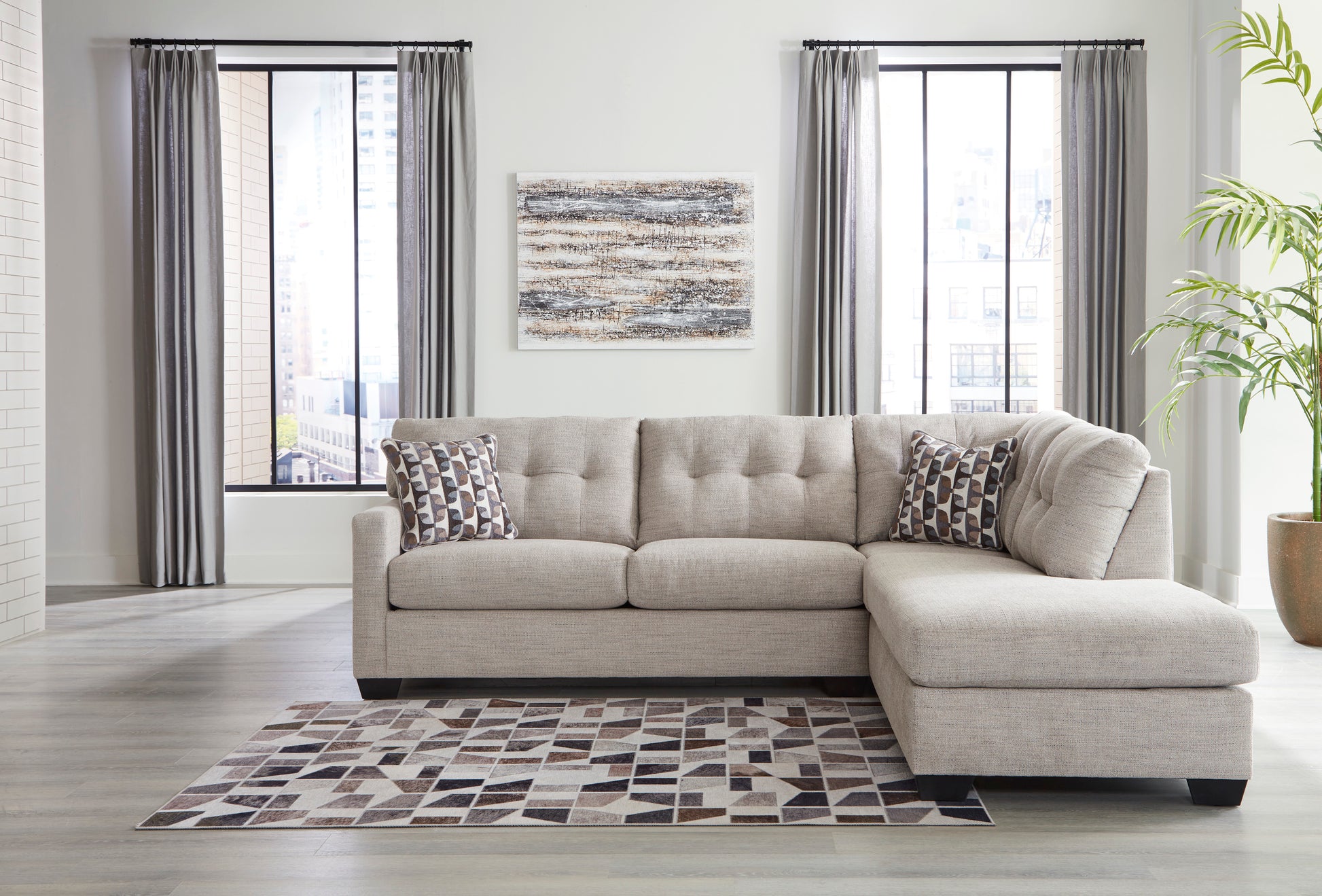 Beige sectional sofa in a living room with a patterned rug and large windows.