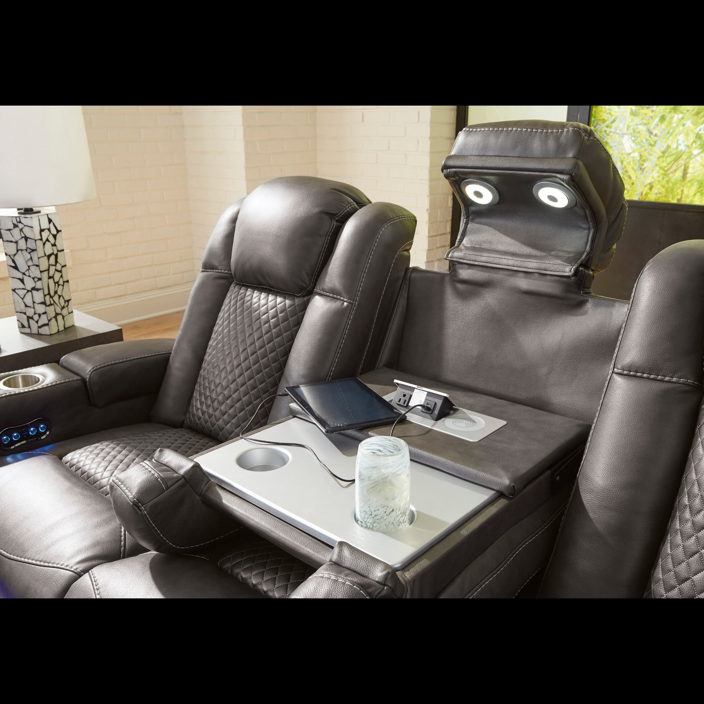 Luxury leather recliner with cup holder, remote control, and small table in a home theater setting.
