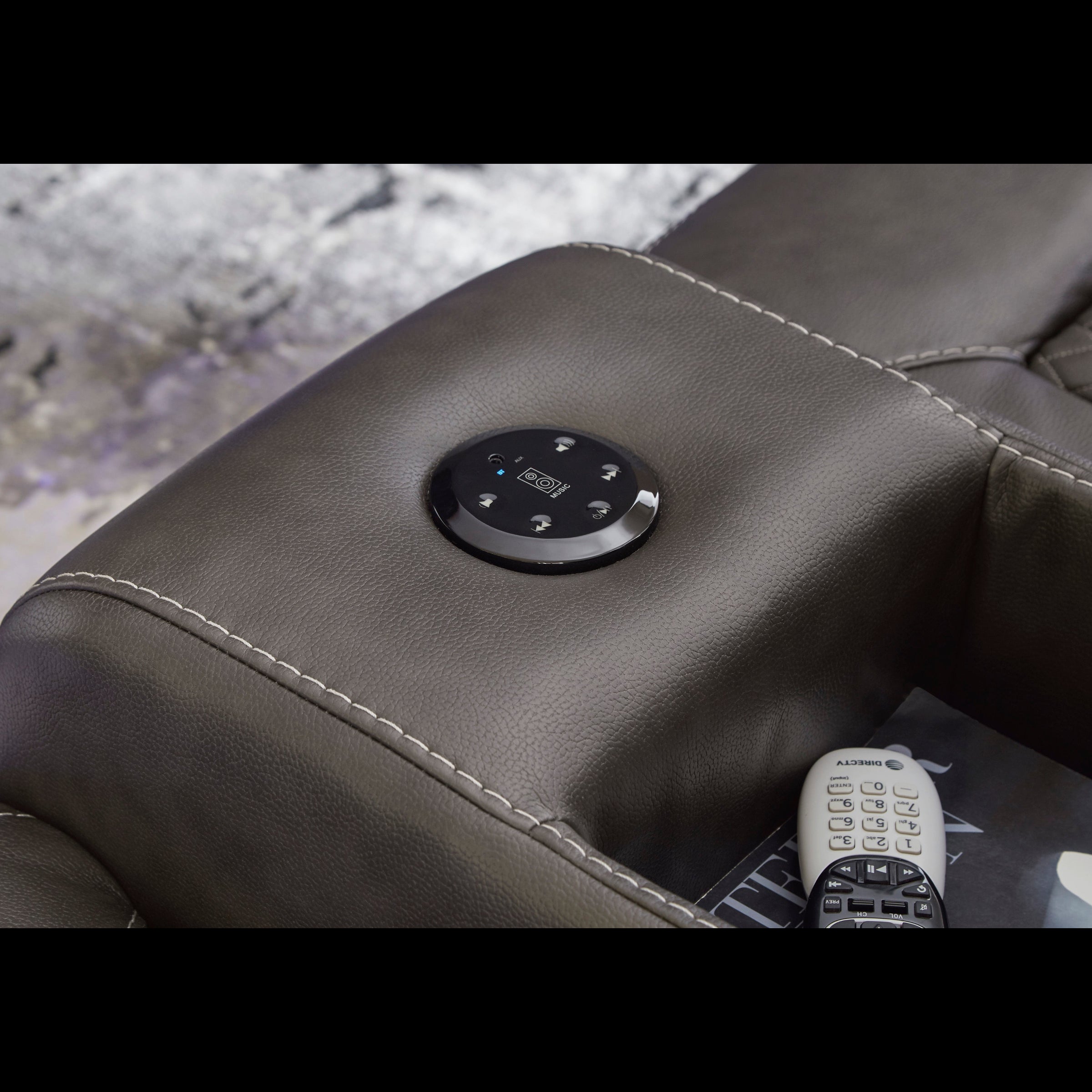 Close-up of a black leather recliner with control panel and remote on a textured surface