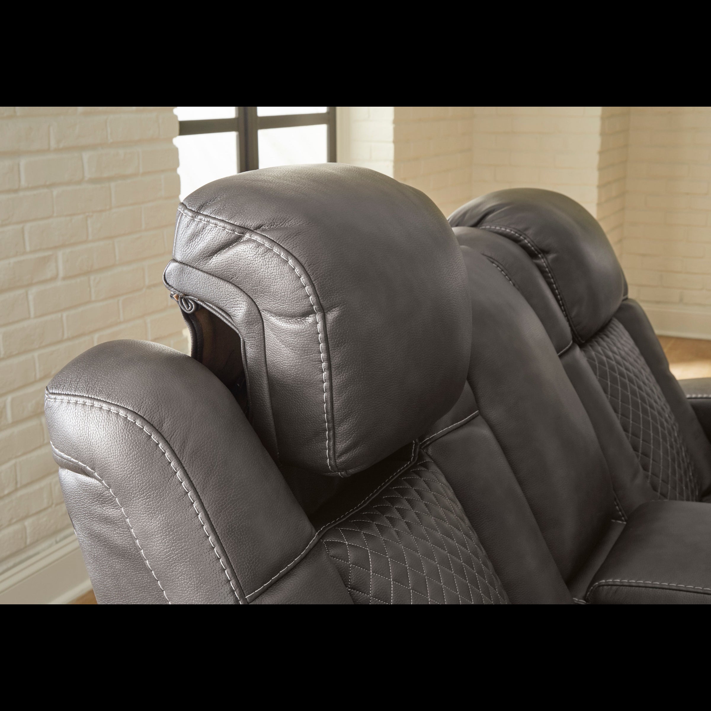 Gray recliner chair with quilted design against a brick wall.