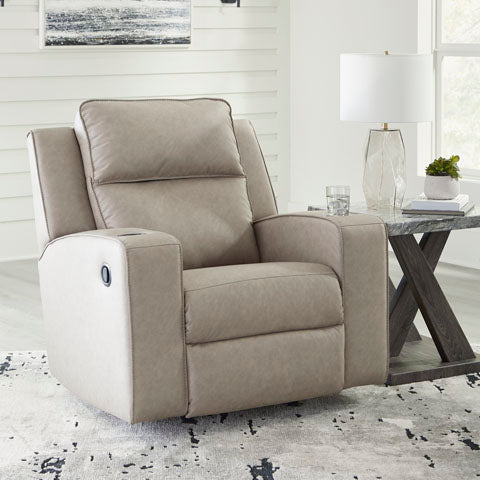 Beige recliner chair in a living room setting with a table and lamp in the background.