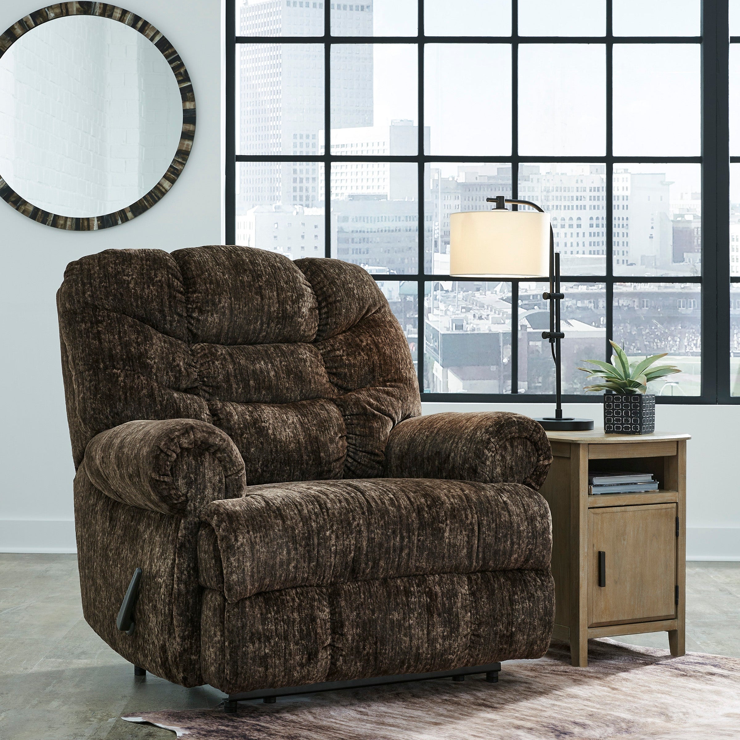 Brown recliner chair in a room with large windows and a lamp.