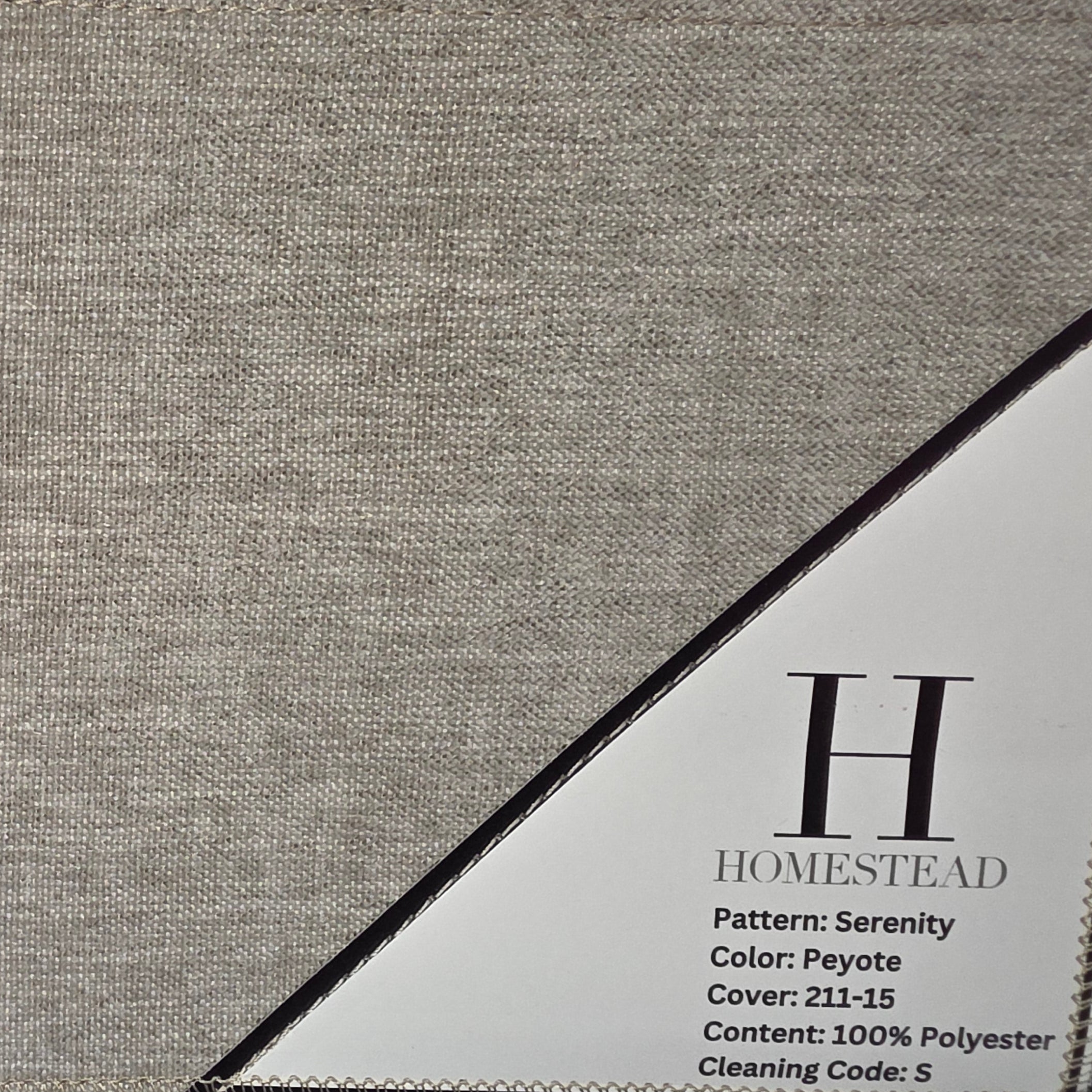 Close-up of a woven fabric swatch in a warm taupe-beige color with a small white product label tag showing the brand 'H Homestead'.