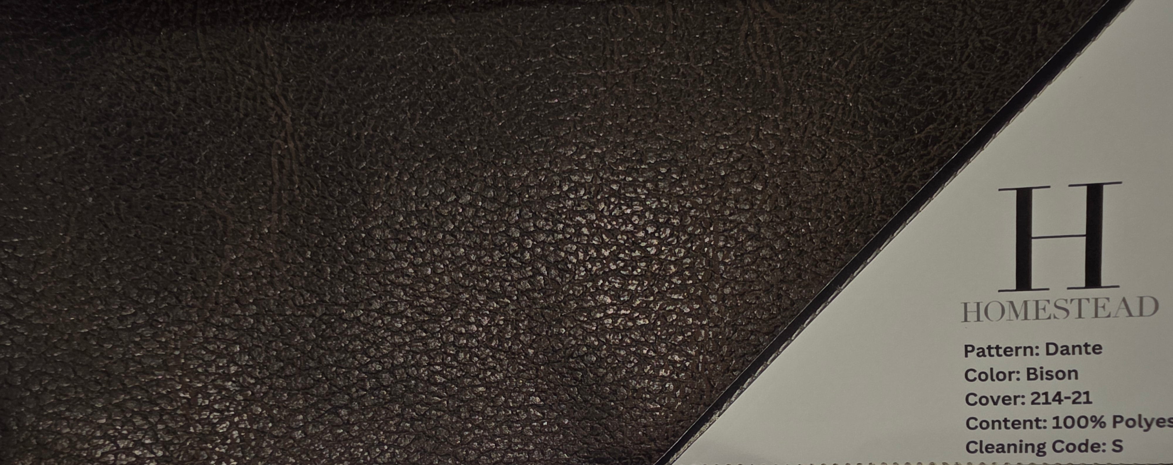 A close-up of a brown textured dog bed with a printed brand label reading 'HOMESTEAD' and pattern/color details, photographed against a window background.
