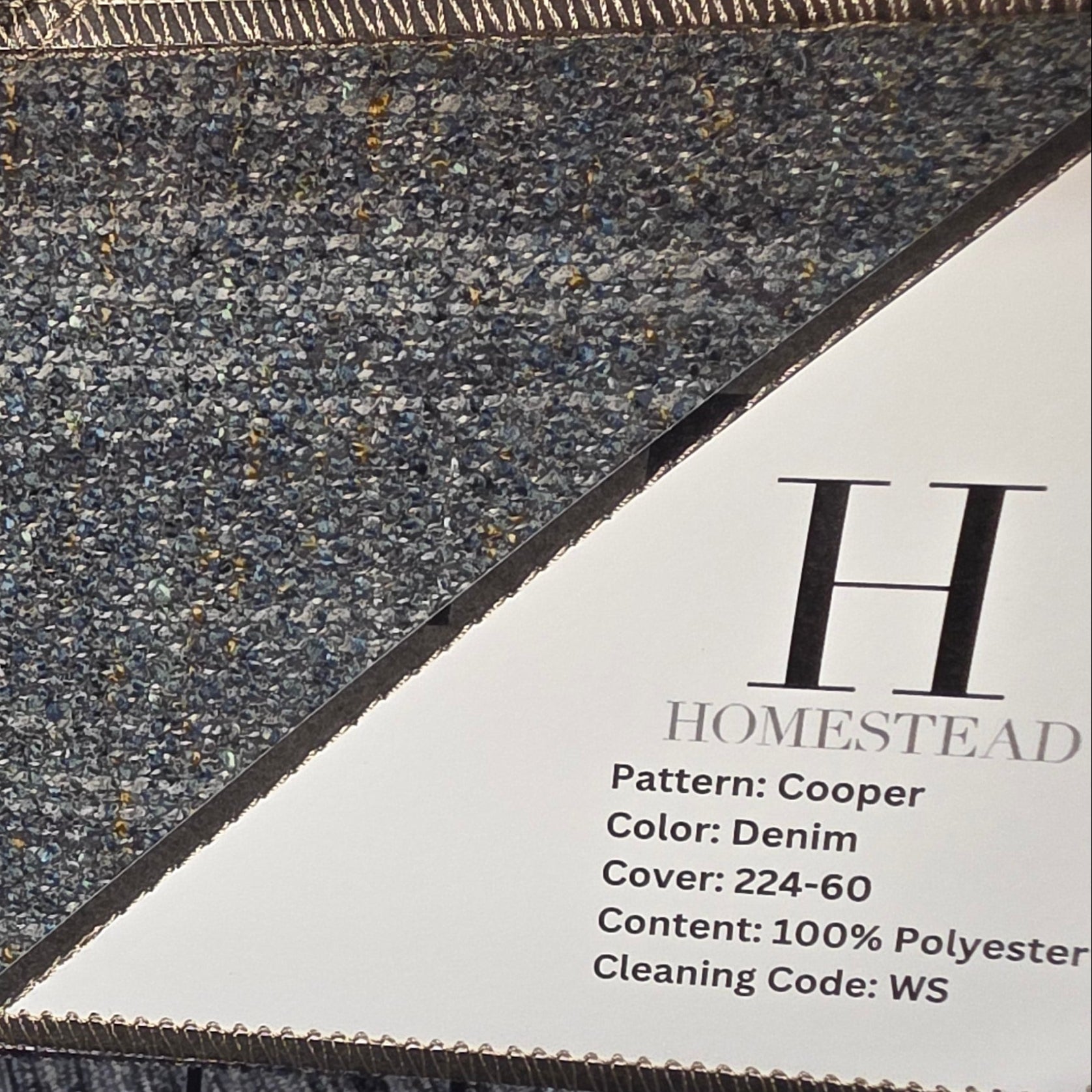 A close-up of a textured area rug sample with a heathered dark gray, brown, and beige pattern, shown hanging in a display rack next to a printed product information card for Homestead Pattern Cooper.