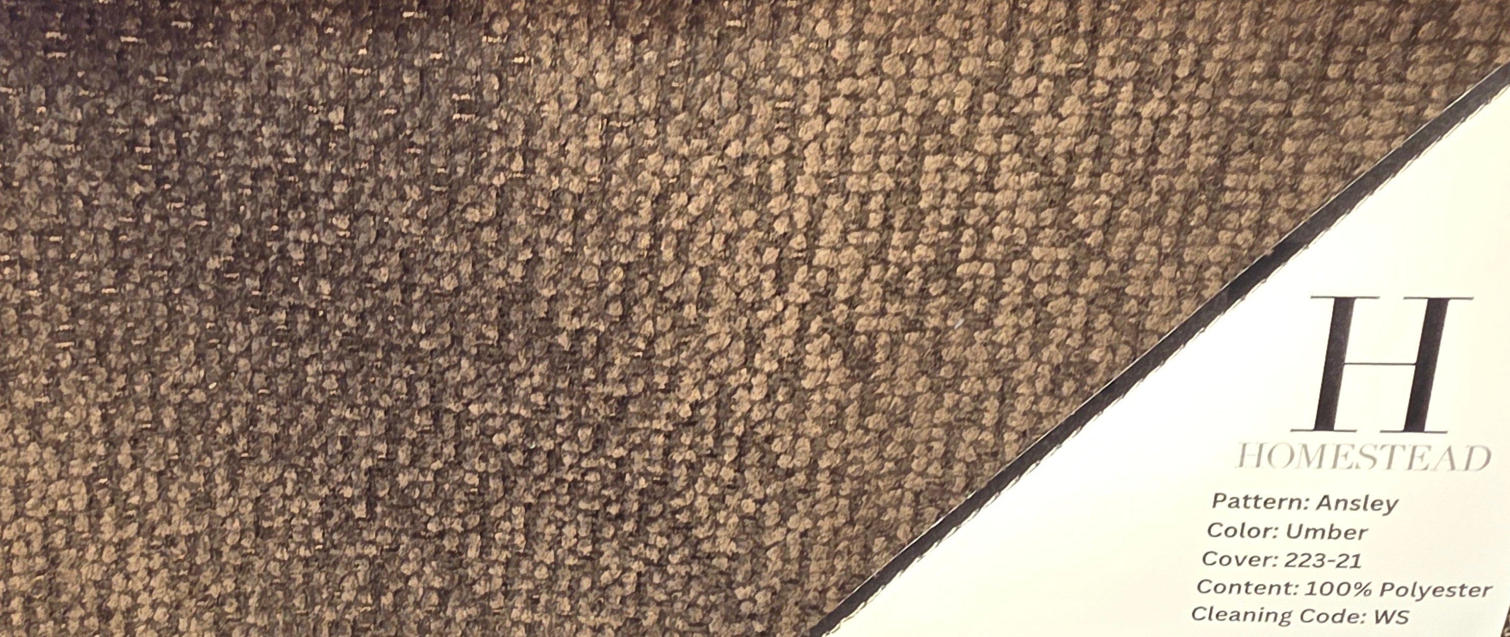 A fabric or carpet sample display showing three pattern/color options stacked vertically, with printed labels including 'HOMESTEAD' and 'Pattern: Ansey', 'Color: Fog', 'Pattern: Ashley', and 'Color: Umber'.