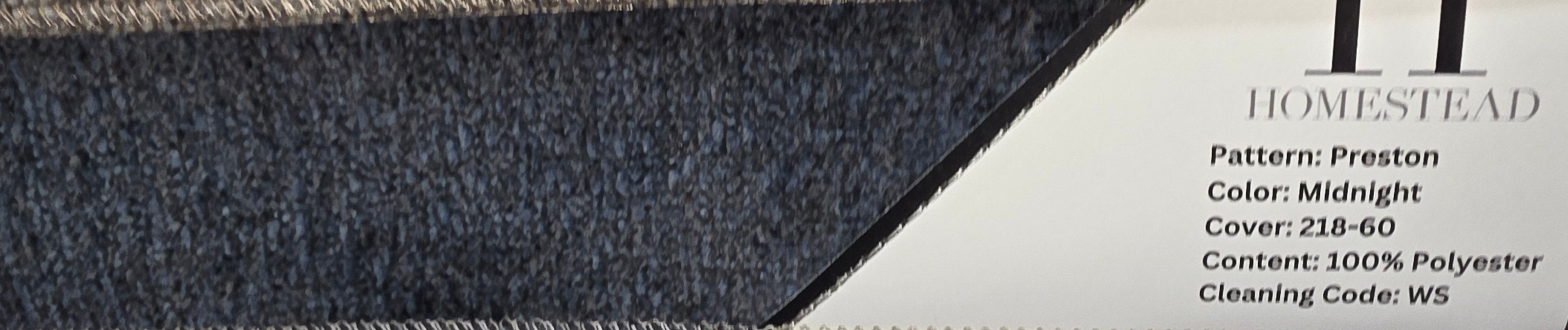 Two carpet samples stacked horizontally on a display rack, with printed labels showing product details. The top sample is labeled Homestead in Taupe and the bottom sample is labeled Homestead in Midnight.