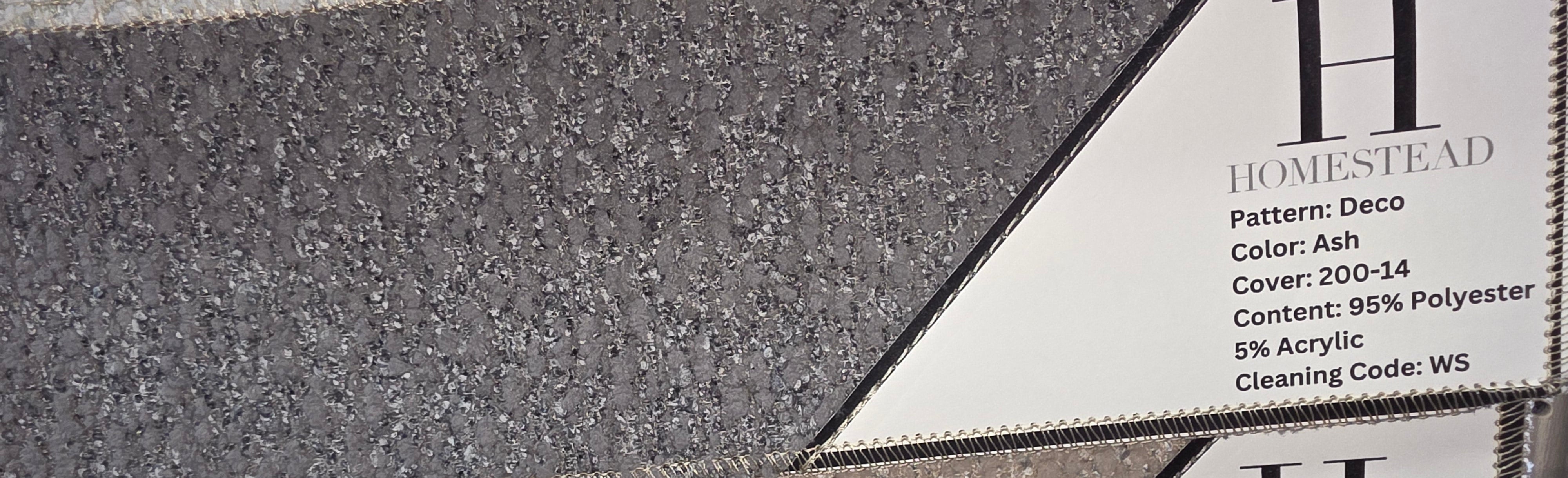 Close-up of stacked Homestead carpet samples with printed labels showing pattern, color, and material details. The visible samples are gray and beige textured carpet in a speckled decoupled pattern.