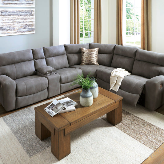 A gray power reclining sectional sofa with an extended ottoman, situated in a room with a light-colored carpet, a picture on the wall, and natural light coming through the windows.