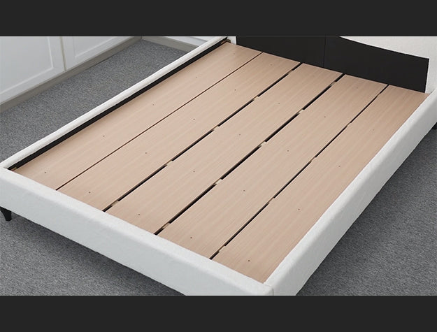 Wooden bed frame with white base on a gray floor